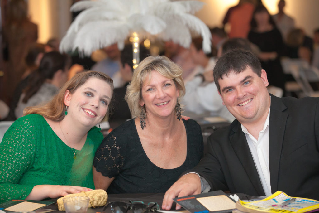 Picture of experts family:
on Left, Young woman wearing a green dress; in middle, white woman wearing a black dress, on right a young white man wearing a white button down shirt & suit jacket.